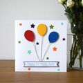 A white square card featuring 1 red, 1 blue and 1 yellow balloon with silver string leading down to a white and lilac banner with the words happy birthday and a child's name. Surrounded by stars of two different sizes in the colours green, turquoise, orange and purple.