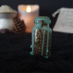 Mini spell jar for good fortune - jar is clear glass containing a mix of herbs and crystals, topped with a cork stopper and sealed with green wax which drips down the sides of the jar
